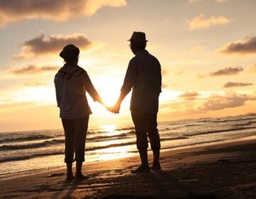 Silhouette couple enjoy elderly relaxation on the beach against sunset or sunrise sky An elderly couple is walking on a beach at sunset holding hands.