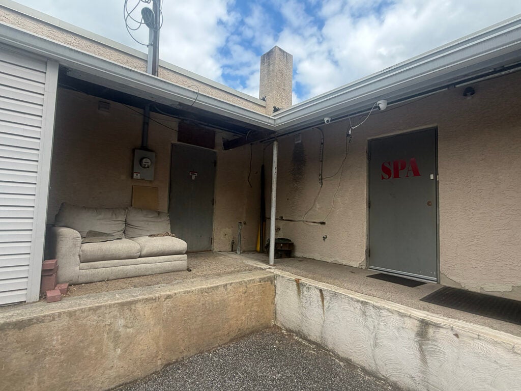 A couch sits outside of a business where two cameras sit above a door with the word "SPA" on it in red letters