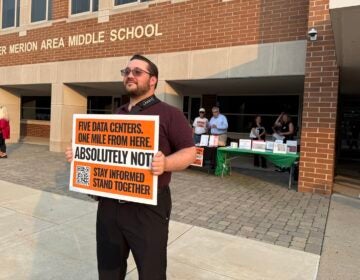 data-center-meeting-zread-2026-08-14-1 A man holds up a sign protesting against data centers outside of the middle school.