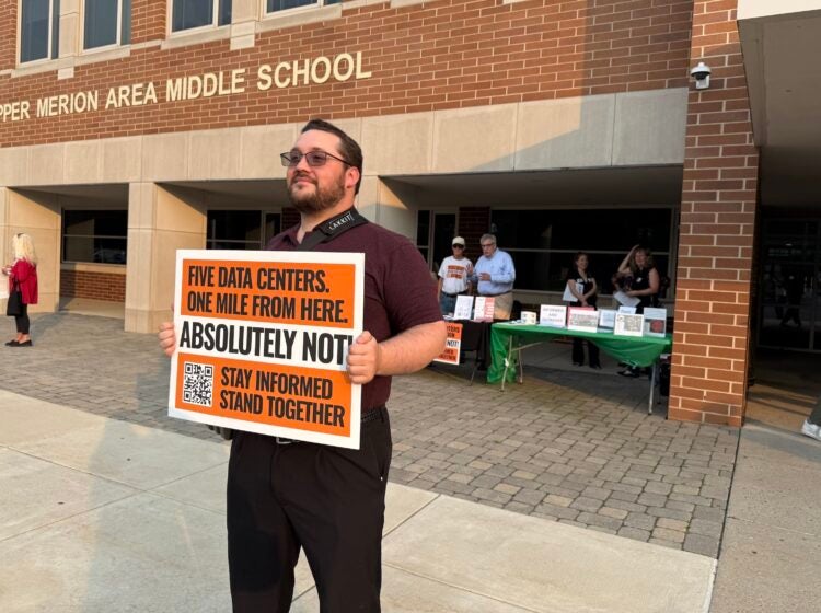 data-center-meeting-zread-2026-08-14-1 A man holds up a sign protesting against data centers outside of the middle school.