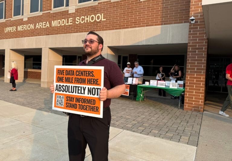 A man holds up a sign protesting against data centers outside of the middle school.