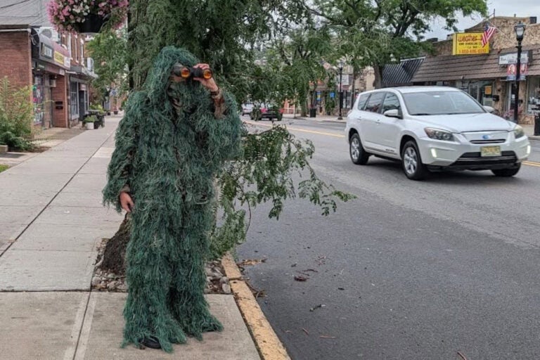A Dunellen Police Department officer dressed as a shrub holding binoculars