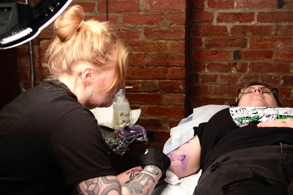 Francesca Decker applying tattoo to Esther Coonfield