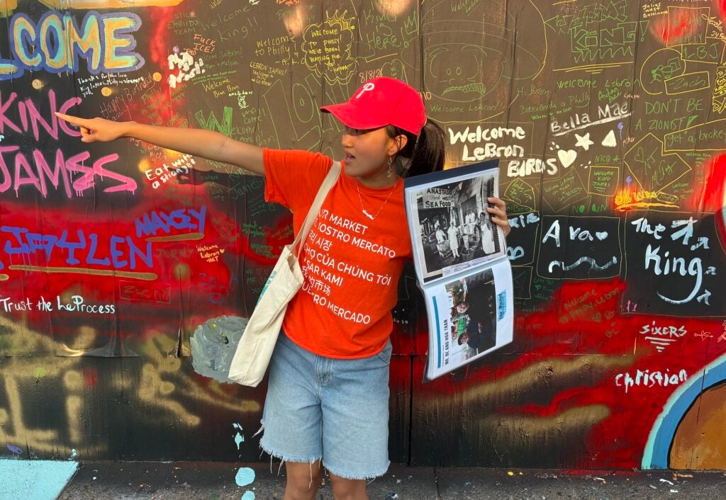 Melissa Yong is holding up a historical photograph as she points out locations during a tour of the Italian Market.