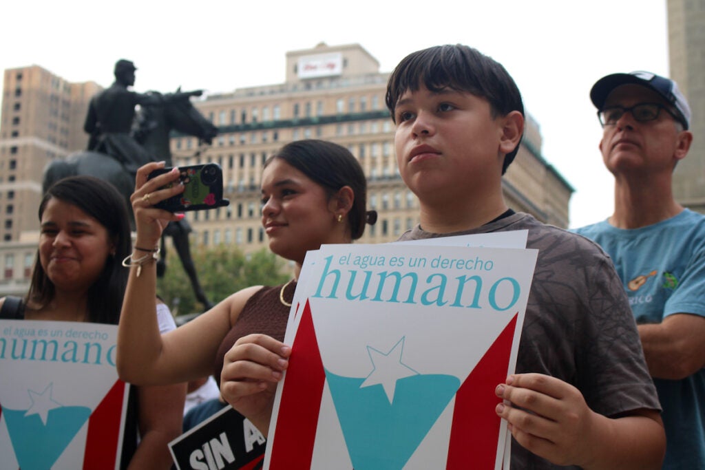 A person holds up a sign that reads, "El agua es un derecho humano"