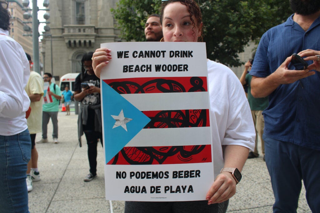 Krystal Rosa holds a sign reading "We cannot drink beach wooder"