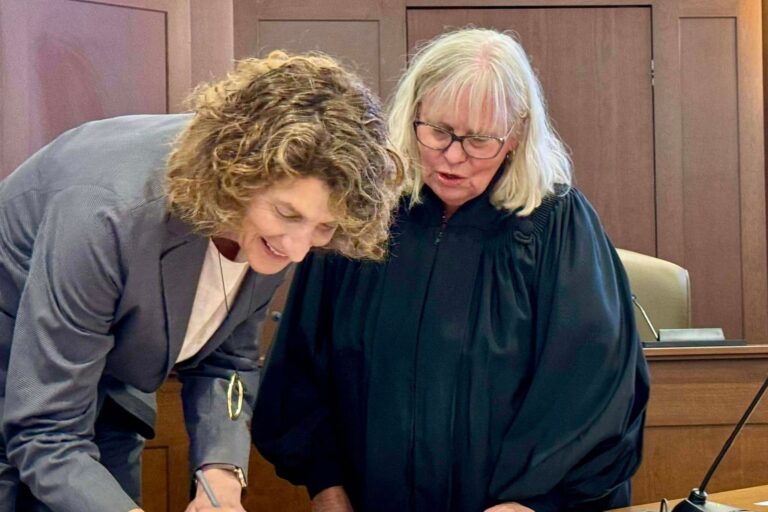 Suzanne Goode signing paper next to a judge