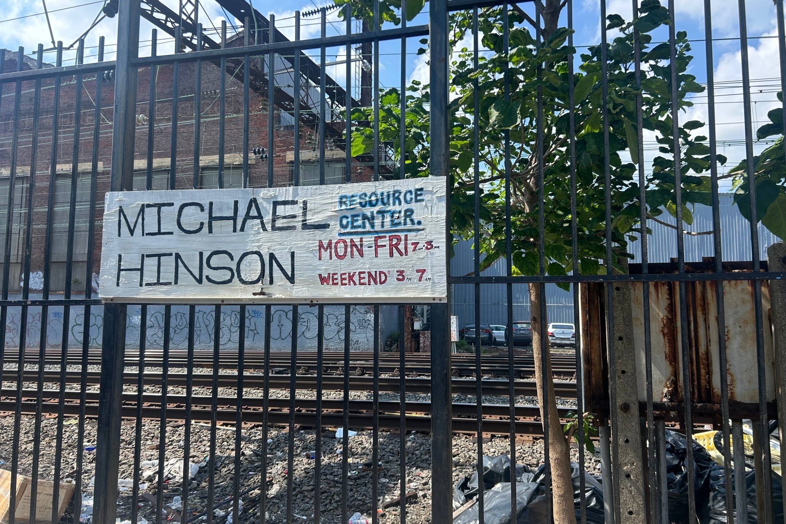 a sign on a fence reads MICHAEL HINSON RESOURCE CENTER. MON-FRI 7 AM TO 3 PM WEEKEND 3 PM TO 7 PM