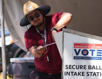 An election worker places a vote-by-mail ballot into a secure bin at the Miami-Dade County Supervisor of Elections Office