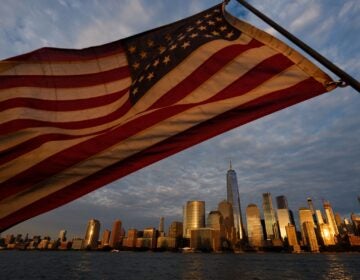 APTOPIX Sept 11 Tribute in Light Test In the foreground, an American flag waves in the air. The skyline of lower Manhattan in NYC is in the background.