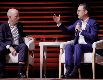 Josh Shapiro speaking into a microphone while sitting on stage in white chairs with Spencer Cox.
