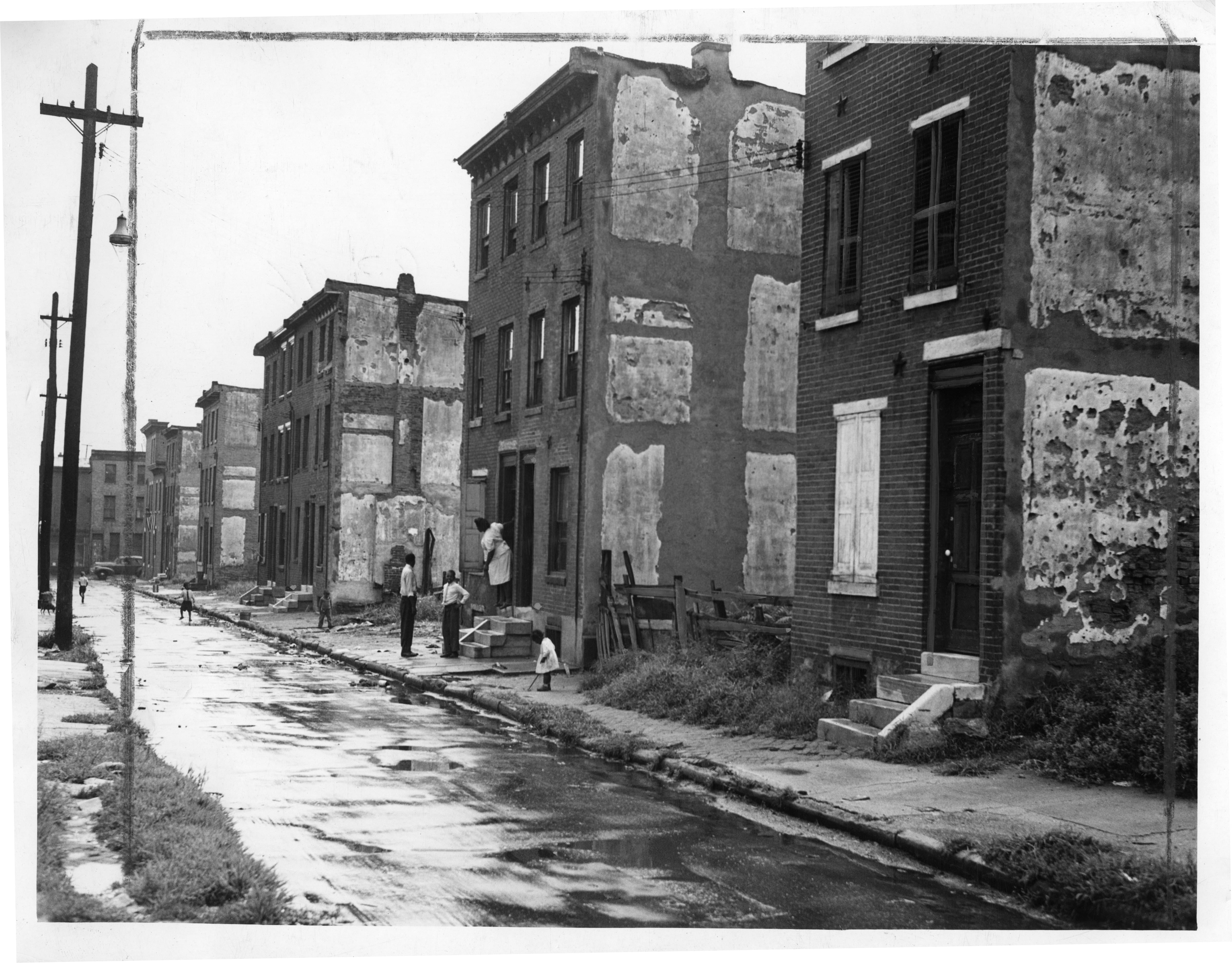 Record Number: 380  Collection: Philadelphia Record Photograph Morgue[V07]  Reproduction restrictions: Unknown  Address: 1500 N. Alder Street Philadelphia, PA 19122, USA  Date of Original: 1945  Image description: Photograph depicts children playing in the street after the rain, while their mother looks on.   