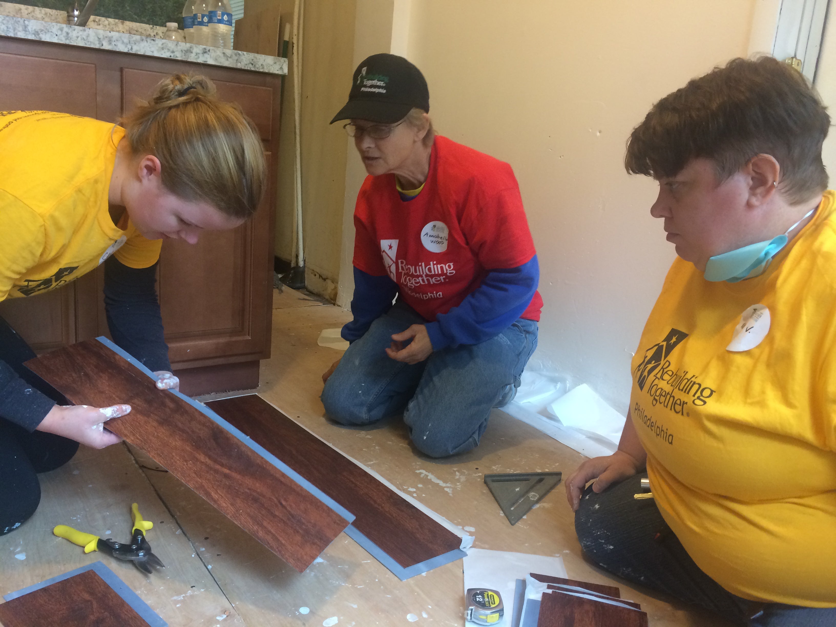 Annabella Wood, 57, (in red) installing new floor on Dawn Anderson’s kitchen, with full-time handywoman Kelly Vincent, 42, and volunteer Kaylin Viales, 23 | Catalina Jaramillo / PlanPhilly