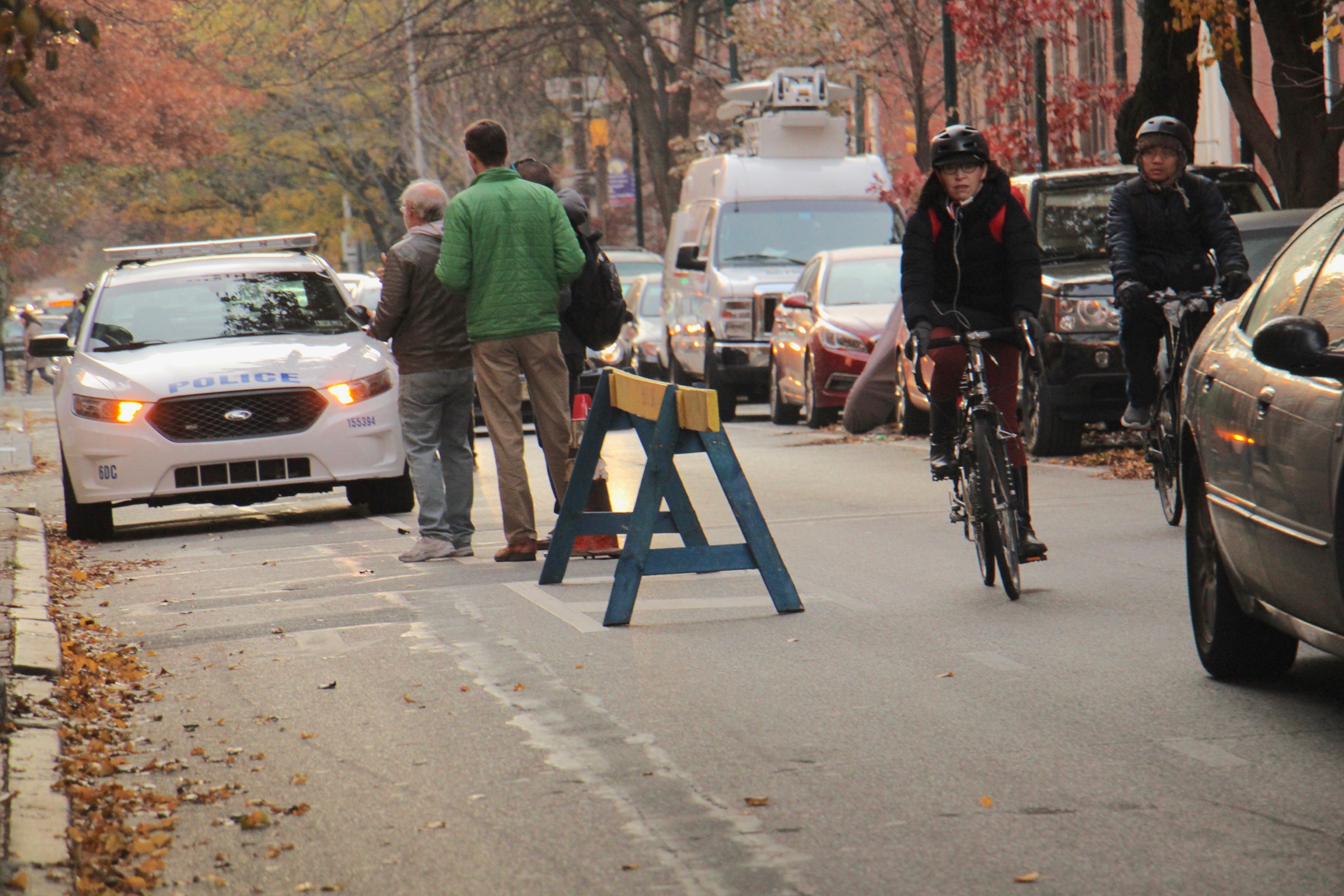 A parked Philadelphia Police car obstructs the bike lane, forcing a cyclist to swerve around into the car lane (Emma Lee, WHYY)