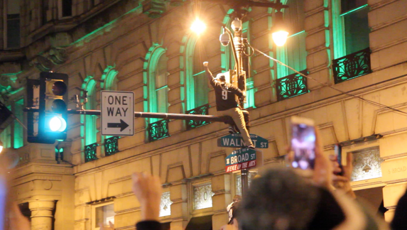 Eagles fan sporting Foles jersey celebrates Philly-style: climbing triumphantly up a light pole on Broad and Walnut. Credit: Kimberly Paynter/WHYY