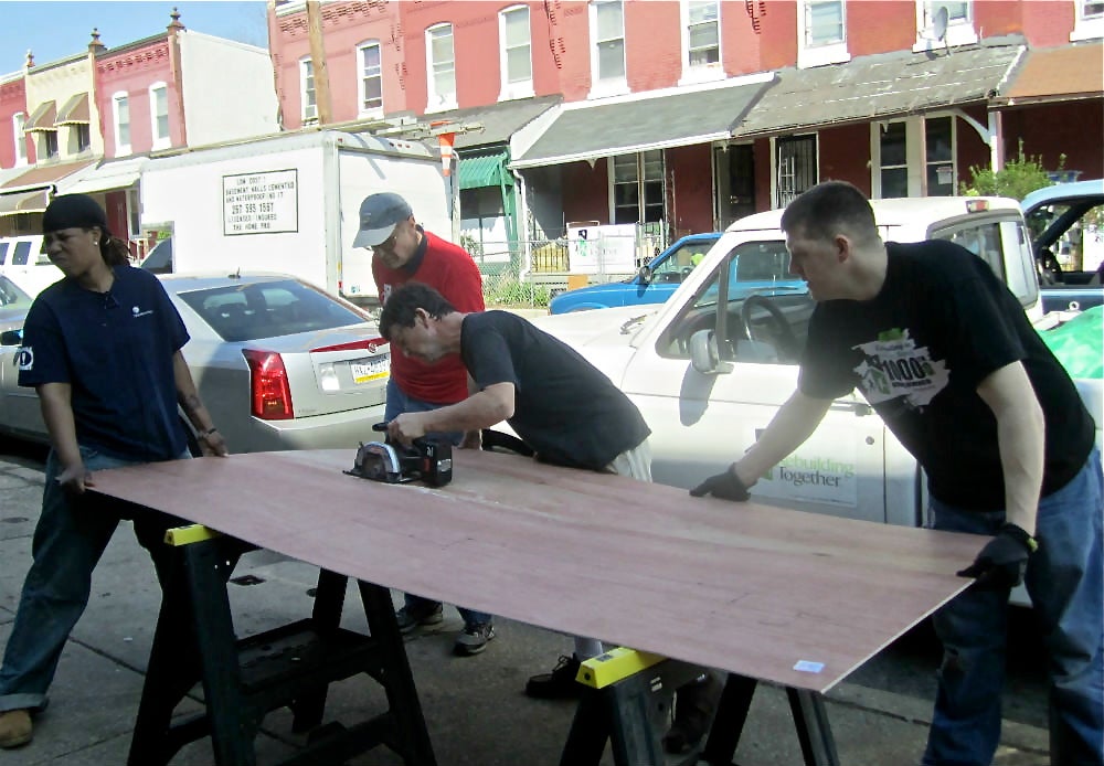 Volunteers brace plywood as it is cut for use in one of the Aspen Street homes. | Christine Fisher Volunteers brace plywood as it is cut for use in one of the Aspen Street homes. | Christine Fisher