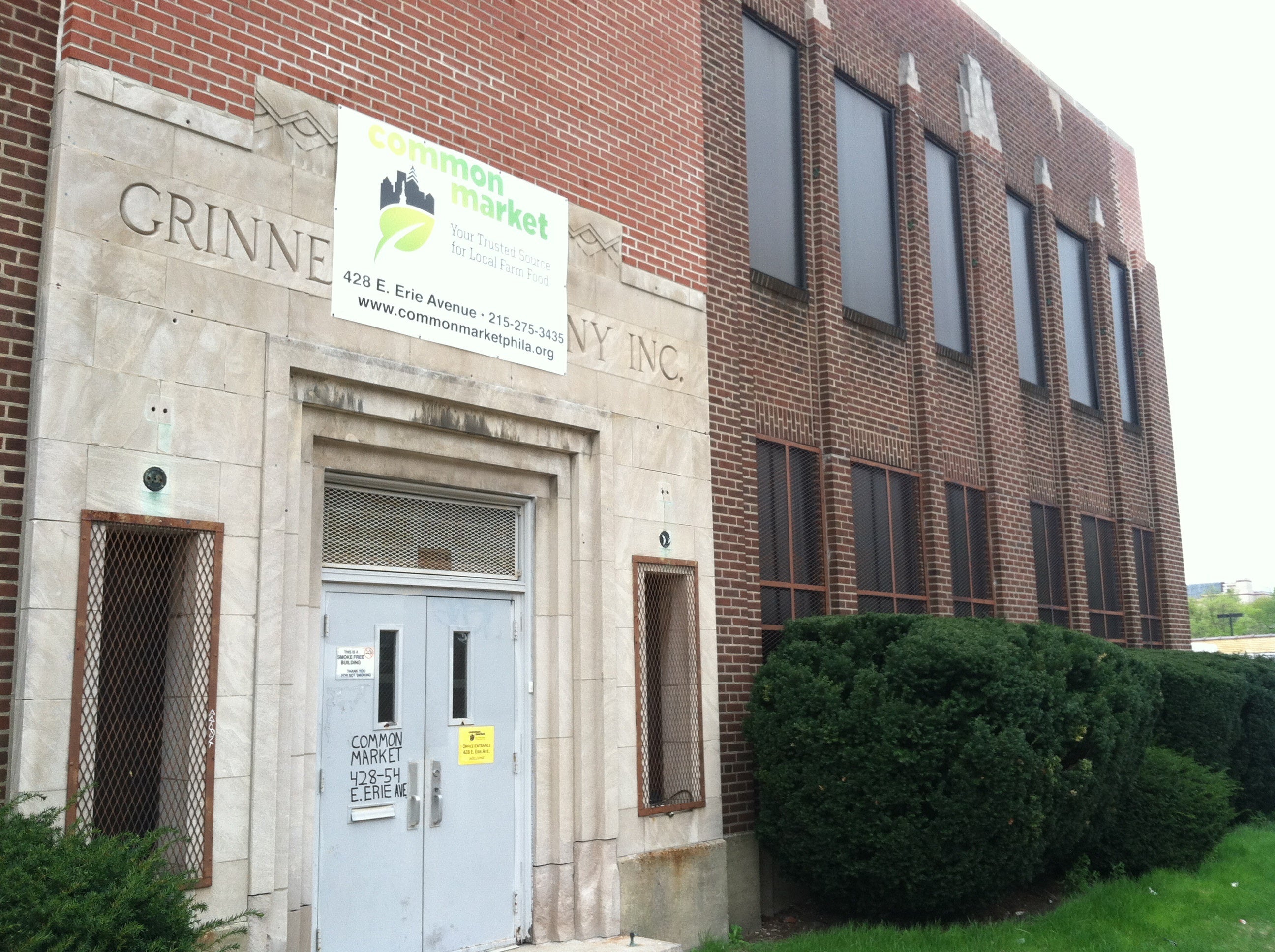 A Common Market sign hangs on the front of the building, where the original building owner's name peeks through