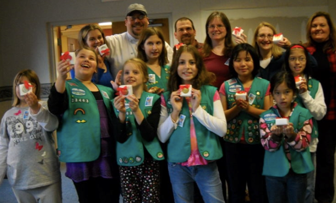 Members and leaders from Junior Girl Scout troops #23463 and #24335 and Wesley Enhanced Living staff showcase the holiday candies they created for distribution to disadvantaged seniors through the Nor