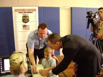 Sen. Mike Stack assists 2nd Police District Officer Mark Mroz in fingerprinting second-grader Gabriel Ortiz.