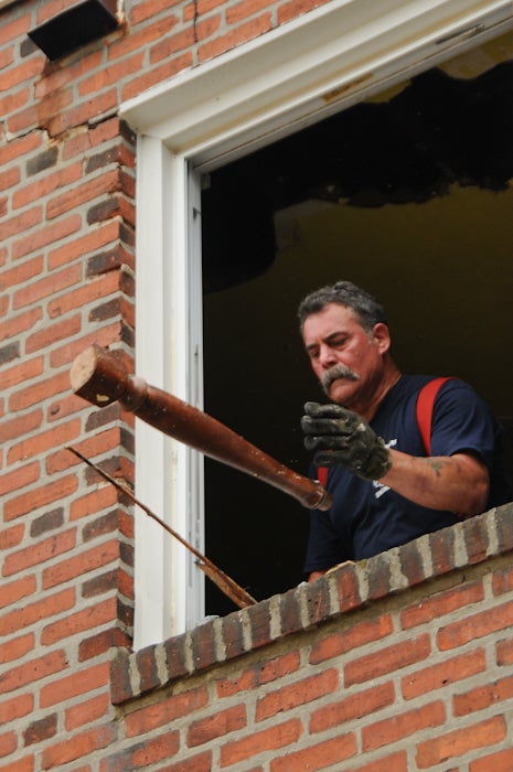 A firefighter tosses debris out of the second story back window of the room, just above the kitchen where the fire started. 